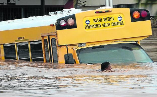 Una persona nada junto a un autobús semihundido para ponerse a salvo en una zona inundada por el ciclón./afp