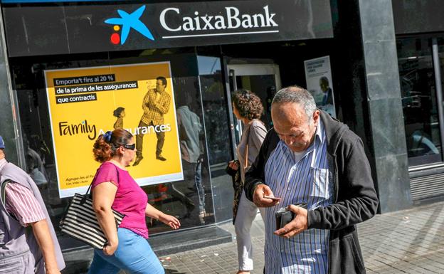 Un hombre guarda dinero ante una oficina de CaixaBank en Barcelona. /reuters