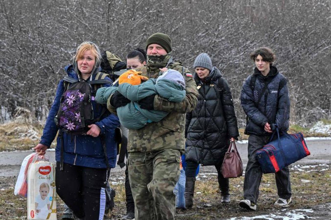 Un soldado polaco lleva a un niño y ayuda a una familia de refugiados después de que estos cruzaran la frontera con Polonia.