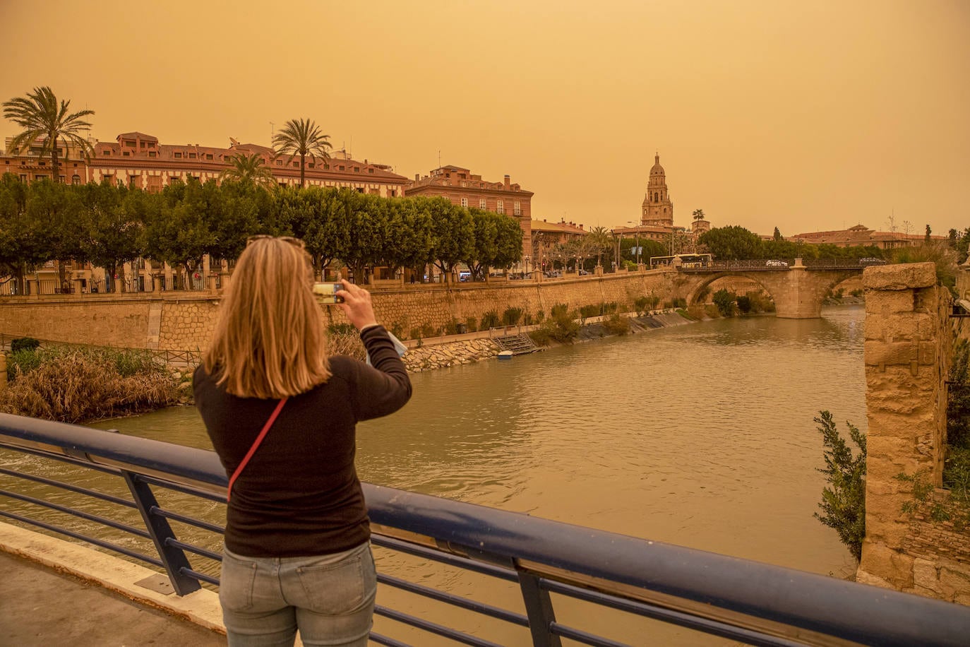 Una mujer hace una fotografía con su móvil del aspecto que presentaba la ciudad de Murcia, con un alto número de partículas y polvo en suspensión que le da ese color anaranjado al cielo. 