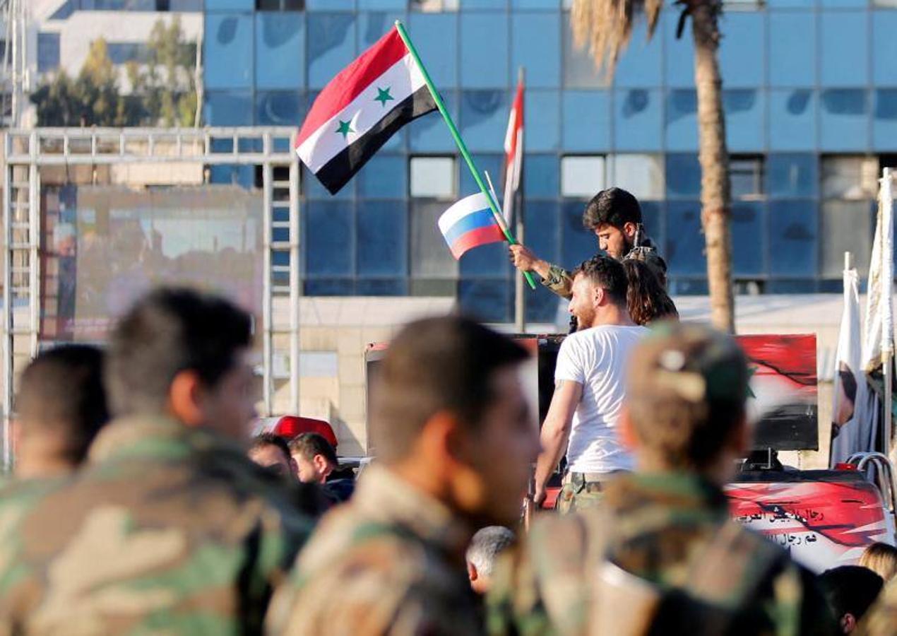 Un soldado sirio ondea banderas rusas y sirias durante una protesta contra los ataques aéreos en Damasco, Siria.