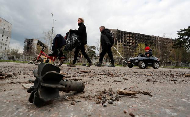 Miembros de una familia transitan por una calle de Mariúpol entre edificios bombardeados y restos de artillería. 