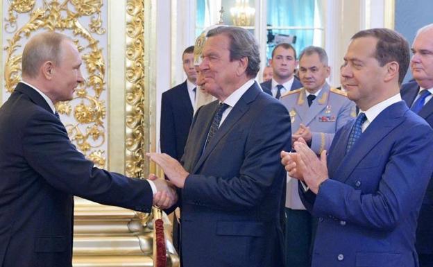 Vladímir Putin estrecha la mano del excanciller y líder socialdemócrata alemán Gerhard Schröeder en presencia del primer ministro ruso Dmitry Medvedev en 2018/Alexey DRUZHININ / AFP
